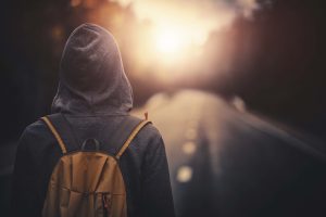 Traveler with backpack walking forward alone at sunset. Stock photo.